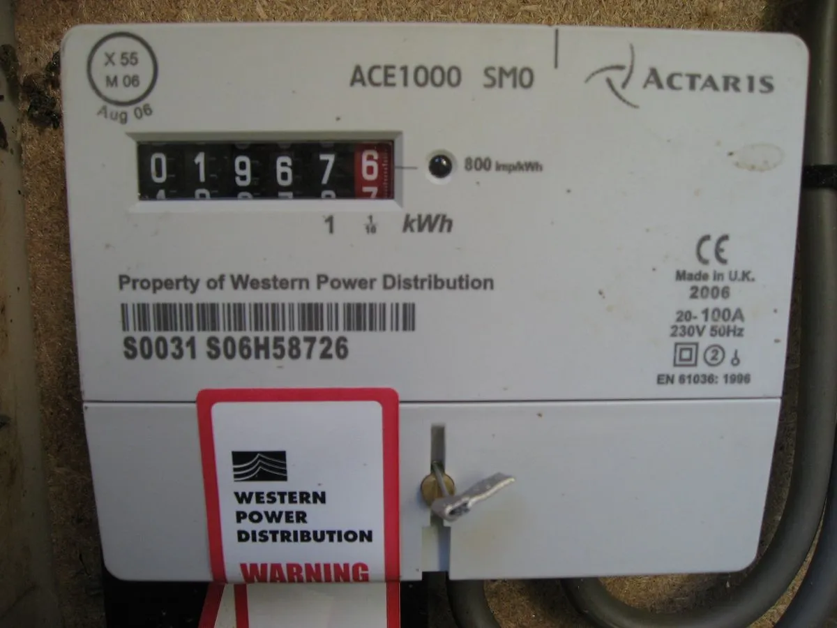 A white electricity meter with a mechanical kWh counter, a barcode and a red seal