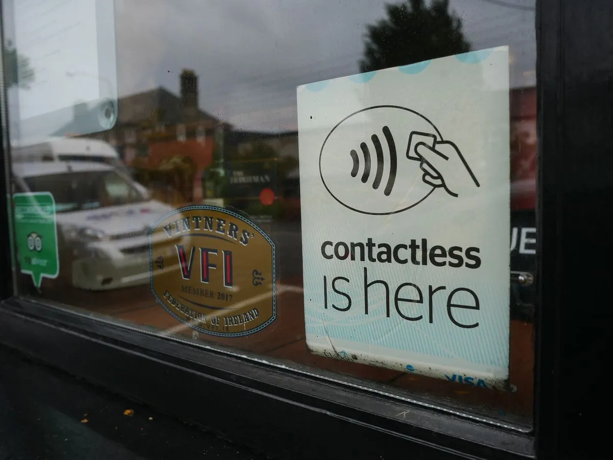 Naklejka z symbolem płatności zbliżeniowej i napisem contactless is here na szybie lokalu