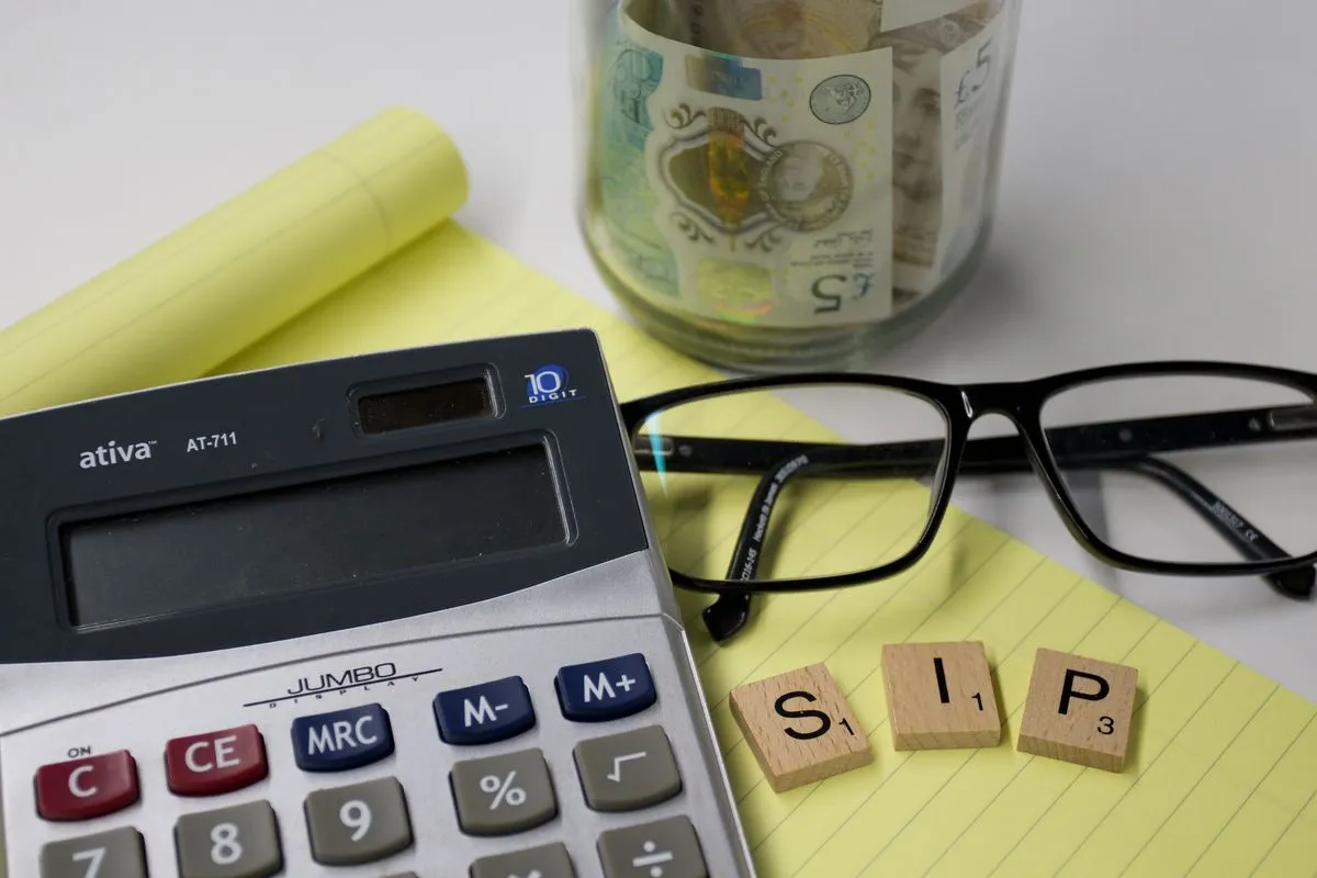 A calculator, glasses, a yellow notepad, wooden letter tiles spelling SIP and a jar of pound notes