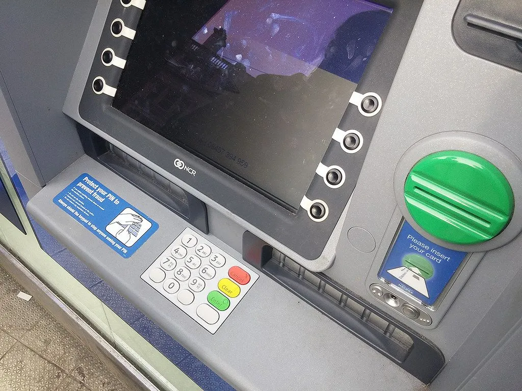 Zbliżenie bankomatu z ekranem, klawiaturą i zielonym otworem na kartę