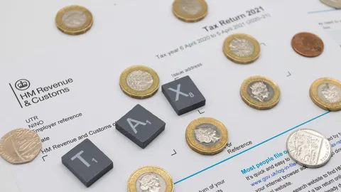 Brytyjskie monety i płytki z literami TAX na formularzu zeznania podatkowego HM Revenue & Customs