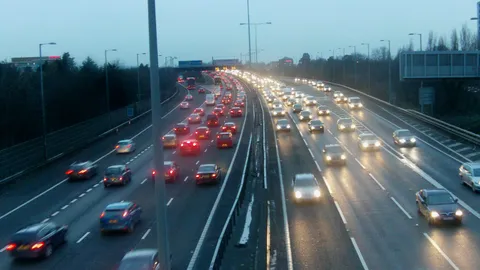 Wielopasmowa autostrada M25 o zmierzchu, sznury samochodów z włączonymi światłami jadą w obu kierunkach