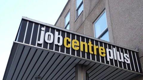 Szyld Jobcentre Plus nad wejściem do biurowca, widziany od dołu