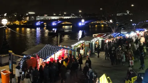Drewniane stragany jarmarku świątecznego ze światełkami nad Tamizą przy Royal Festival Hall, w tle Waterloo Bridge nocą