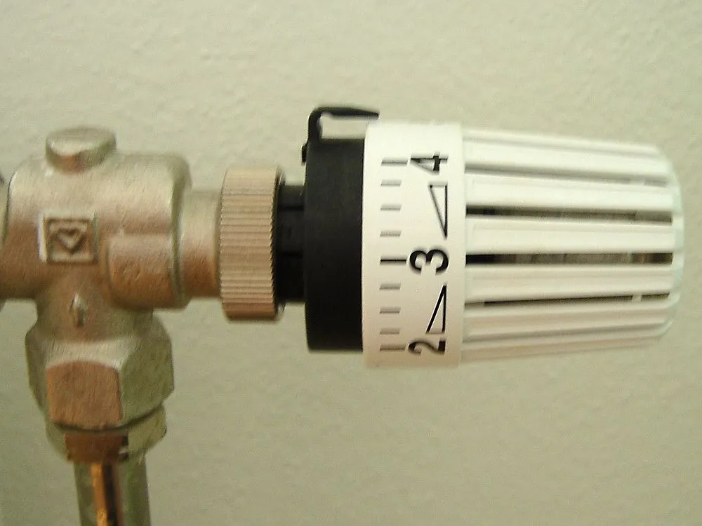 A white thermostatic radiator valve head with a scale from 2 to 4, fitted to a metal valve