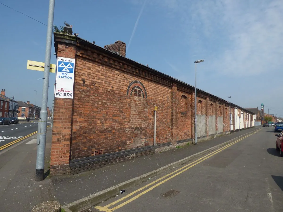 A brick garage building on a street corner with a blue MOT sign showing three white triangles and the words MOT Station