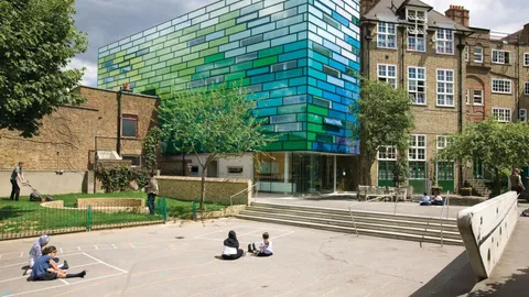 Plac szkoły podstawowej Clapham Manor w Londynie z kolorowym, przeszklonym budynkiem i starą ceglaną szkołą